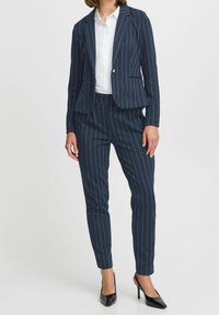 Granatowy garnitur w prążki z dopasowaną marynarką i wąskimi spodniami, w połączeniu z białą koszulą i czarnymi szpilkami. Tkanina o fakturze, elegancki design.