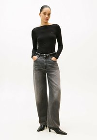 Top lungo a maniche lunghe nero a coste, jeans grigi a gamba larga a vita alta e décolleté neri a punta. Caratteristiche di design principali includono una cintura e tasche.