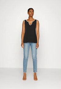 Top preto sem mangas com acabamento branco, decote em fenda; combinado com jeans azul claro ajustados e sandálias castanhas com tiras. Corte simples e reto.