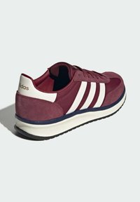 Baskets Adidas bordeaux avec des rayures blanches, patch blanc au talon avec logo, bordure de la semelle intermédiaire bleu marine et semelle extérieure noire sur fond uni.