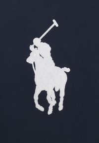 Witte geborduurde silhouet van een polo speler op een paard met een omhoog gehouden hamer op een donkere marineblauwe achtergrond.
