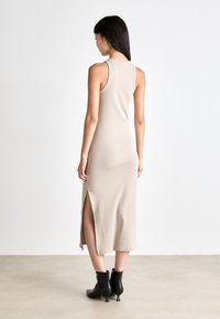 Rochie midi bej, fără mâneci, cu o fanta laterală; formă ajustată, textură în dungi, design minimalist. Purtați cu cizme negre până la gleznă.