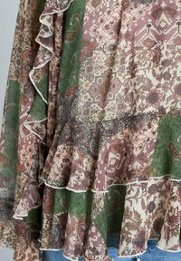 Blusa in tessuto con stampa floreale e volant, con tonalità di verde, bordeaux e crema. Stampa testurizzata con aree di contrasto ben distinte.