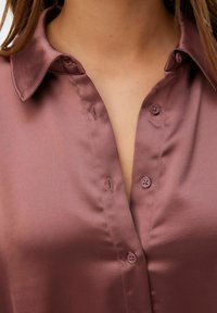 Satin skjorte med knaplukning i mauve med krave og en stolpe med fire knapper, der fremhæver den glatte, blanke tekstur.
