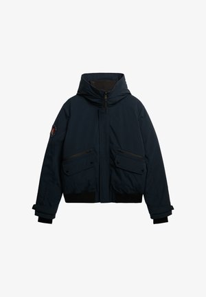 Donkerblauwe gewatteerde jas met capuchon, ritssluiting, twee voorzakken en geribbelde manchetten. Voorzien van een logopatch op de mouw. Waterdicht materiaal.