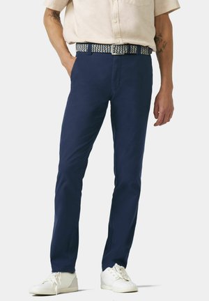 Marineblauwe katoenen broek met een slim fit. Voorzien van een patroon geweven riem. Draagt een wit paar sneakers en een lichtgekleurde shirt met korte mouwen.