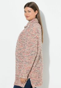 Oversized stickad tröja i beige med flerfärgade inslag. Har hög hals, långa ärmar och sidslitsar för en avslappnad passform.