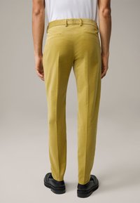 Gele corduroy broek met een rechte pasvorm, voorzien van twee achterzakken en riemlussen, gecombineerd met zwarte schoenen.