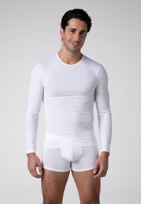 Camicia bianca a maniche lunghe e slip attillati, realizzati in tessuto liscio. Entrambi presentano un design semplice e senza cuciture, privo di motivi.