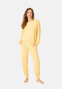 Felpa gialla con vestibilità morbida e maniche lunghe, abbinata a pantaloni jogger coordinati con vita elastica e polsini.