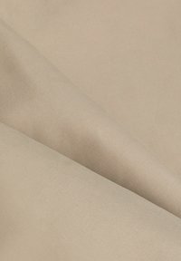 Tissu en coton beige avec une surface lisse et légèrement texturée, présentant de subtiles nervures diagonales et des plis doux.