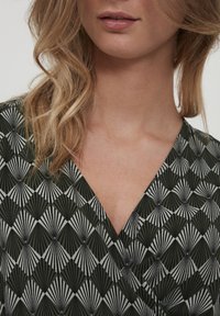 Grönmönstrad textil med en geometrisk design som har fläktformer i svart och vitt, placerad i en V-ringad plagg. Mjuk textur.