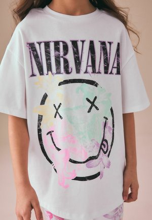 Fehér, bő szabású póló lila "NIRVANA" felirattal és egy kopott hatású mosolygós arc logóval, amelyet pasztell színű virágok díszítenek.