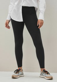 Svarta leggings i stretchigt material, kroppsnära design, slät textur, ihop med ljusfärgade sneakers med svarta snören och detaljer.