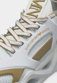 Λευκό και μπεζ αθλητικό παπούτσι Emporio Armani EA7 με λεπτομερείς κορδόνια, πλέγμα πάνελ και λογότυπο της μάρκας στο πλάι και στη γλώσσα.