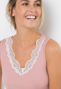 Haut rose clair avec un col en dentelle festonnée. Le tissu est lisse avec un design ajusté, mettant en valeur les délicates accents en dentelle blanche.