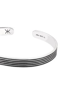 Silvrig manschettarmband med horisontella svarta ränder, stämplad insidan med "JGJ 925 Ag" och en geometrisk symbol i motsatt ände.