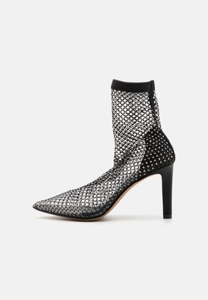 Black mesh ankle boot with pointed toe, stiletto heel, and decorative stud accents. Features a stretchy sock-like upper design.