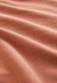 Tekstil med en blød, krøllet overflade; dæmpet terracotta farve med en glat, ensartet struktur. Synlige vævede mønsterdetaljer.