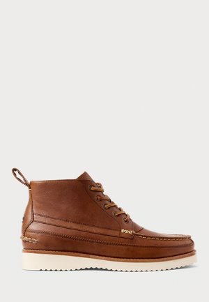 Brown leather ankle boot with cream rubber sole, lace-up front, moc toe stitching, and pull tab at back, shown in profile on white background.