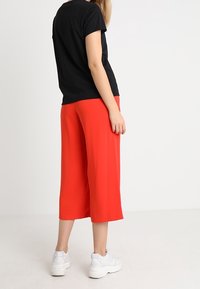 Czarny t-shirt z krótkim rękawem w połączeniu z jasnoczerwonymi kulotami, prezentujący luźny krój, gładką teksturę oraz białe buty sportowe.