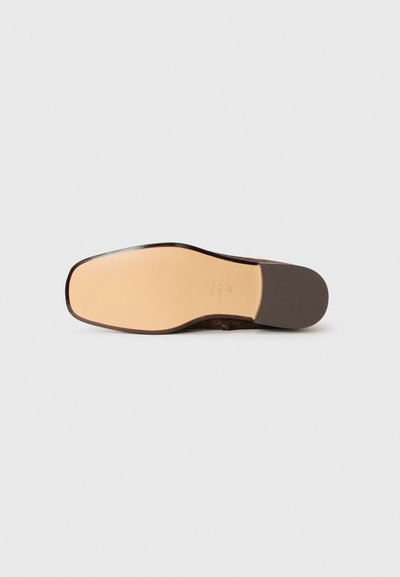 Brun mockaskosole med en slät beige mittdel, rund tå och en kontrasterande mörk kant, med subtil präglning nära hälen.