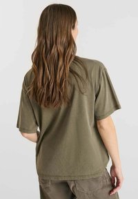 Olijfgroene katoenen t-shirt met een relaxte pasvorm, korte mouwen en een ronde zoom, gecombineerd met gestructureerde bruine broeken.