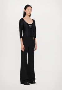 Body negro de manga larga con escote en forma de barco y detalle de logo, combinado con pantalones anchos negros que cuentan con una hebilla decorativa.