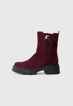 Burgundy suede ankle boots with a chunky black sole, elastic side panels, and a decorative silver buckle accent on the upper.