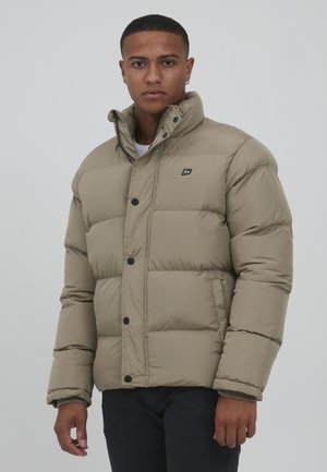 Beige pufferjack met een geborduurd ontwerp, ronde kraag en zwarte knopen. Heeft een klein logo op de borst en een ritssluiting.