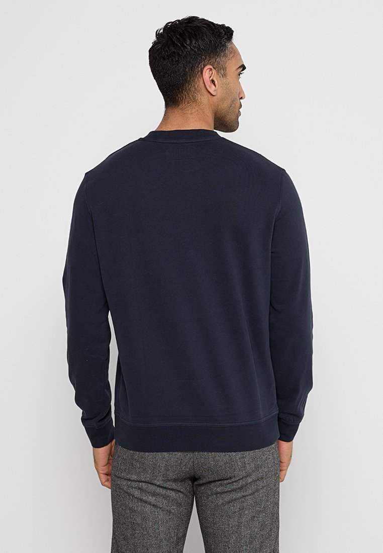 Sweatshirt bleu marine avec un col rond, des manches longues et un ourlet côtelé. Fabriqué en tissu doux, il présente une texture lisse et un design minimal.