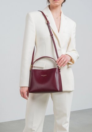 Sac à main en cuir bourgogne avec une forme structurée, une poignée supérieure et une longue bandoulière réglable. Présente un détail de logo en or sur le devant.