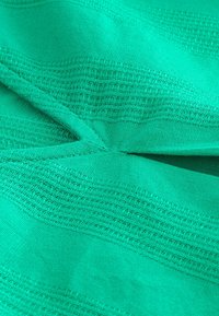 Tessuto di un verde vibrante con strisce verticali testurizzate e aree lisce. Tessuto morbido e leggero che mostra un motivo intrecciato.