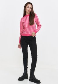 Różowy sweter w wzór houndstooth z długimi rękawami i okrągłym dekoltem, zestawiony z czarnymi skinny jeansami i czarnymi botkami. 
