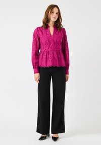 Fuksia brodert bluse med peplum liv, lange ermer og scallop-kant, parret med svart høyt liv bukser og hæler.