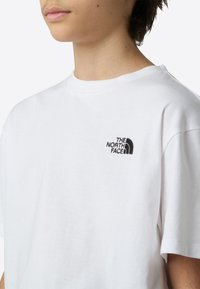 Bela bombažna majica s črnim vezenim logotipom "The North Face" na levi strani prsnega koša. Kratki rokavi in okrogel izrez na vratu.