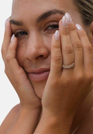 Roze-gouden ring met meerdere heldere, rechthoekige edelstenen, gedragen aan een hand met natuurlijke nagels, tegen een neutrale achtergrond.