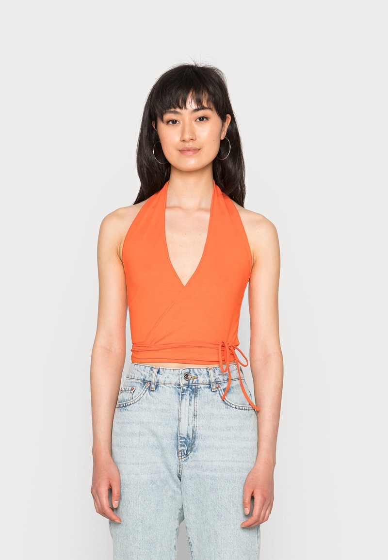 Top de halter em laranja brilhante, com decote V profundo e design envolvente, feito de tecido macio. Combinado com jeans de denim claro de cintura alta.