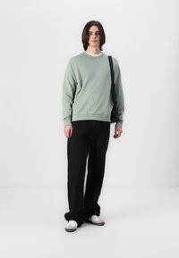 Mintgrøn sweatshirt med ribbede manchetter og kant, parret med løse sorte bukser. Hvide sneakers afslutter looket. En simpel skuldertaske bæres.