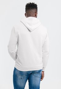 Witte hoodie met een achteraanzicht, voorzien van een capuchon met trekkoord, lange mouwen en geribbelde manchetten, gecombineerd met een blauwe spijkerbroek. Soepele textuur.