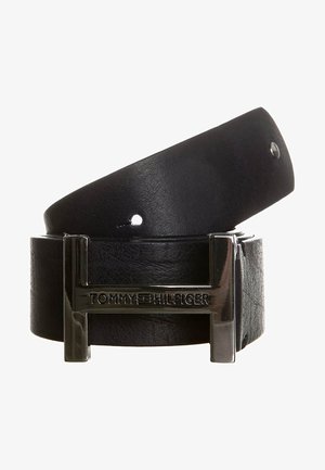 Sort læderbælte rullet sammen med en skinnende sølvfarvet rektangulær spænde med indgraveret tekst "Tommy Hilfiger".