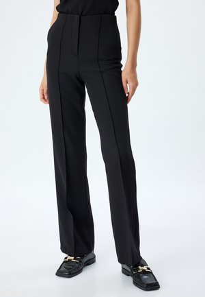 Pantalones negros ajustados con una cintura alta, diseño de pierna recta y costuras frontales prominentes. La tela parece suave y estructurada.