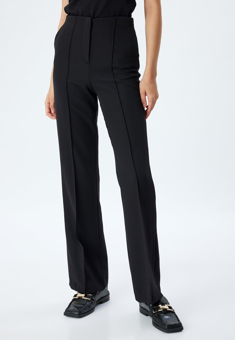 Zwarte op maat gemaakte broek met een hoge taille, rechte pijpen en opvallende voornaad. De stof lijkt glad en gestructureerd.
