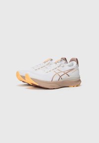 Weiße Sportschuhe mit einer strukturierten Oberseite, orange und braune Akzente sowie einer dicken beigen Sohle. Ausgestattet mit Schnürsenkeln und Branding auf der Zunge.