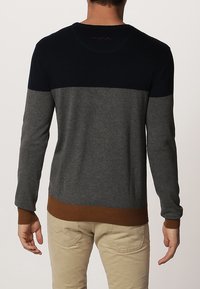 Stickad tröja med en marinblå övre del, grå mittsektion och brunt ribbat nederkant. Långa ärmar och rundad halsdesign, mjuk textur.