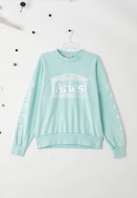 Pulover mint verde cu guler rotund, tiv și manșete cu dantelă. Prezintă text alb „Aries” și grafică sub formă de coloane pe partea din față și pe mâneci.