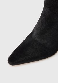 Fekete, hegyes orrú csizma, puha, sima anyagból készült, amely elegáns formatervezésű, enyhén textúrázott felülettel rendelkezik.