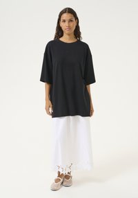 Sort oversized t-shirt med korte ærmer, parret med en hvid maxiskirt med scallopped blondekant i bunden, båret med lyse sko.
