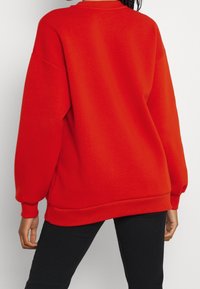 Röd oversized sweatshirt med långa ärmar, ribbade muddarna och en enkel rundad halsringning. Mjuk bomullsstruktur och avslappnad passform.