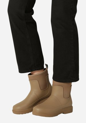 Botas de tobillo de goma en color beige con un panel elástico marrón, punta redondeada, suela texturizada y una lengüeta en la parte posterior para facilitar su puesta.